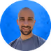 Smiling bald man with a beard against a bright blue background.