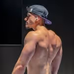 Muscular man wearing a backward cap shows his back and shoulder muscles against a dark background.
