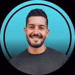 Smiling man with short dark hair and beard wearing a black shirt against a turquoise background.